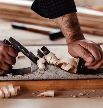 Carpenter's hands planing a plank of wood with a hand plane close up